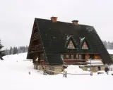 Drewniana bacówka w zimowej scenerii, otoczona śniegiem i lasem.