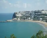 En vit stad klättrar uppför en klippa vid havet i Puglia, Italien. En strand och en hamn syns nedanför.