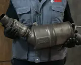 Mechanik w rękawiczkach trzyma zużyty fap, element układu wydechowego.