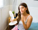 Femme examinant son visage dans un miroir lumineux, cherchant des conseils sur comment maigrir du visage.