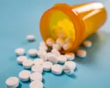Białe tabletki rozsypane z pomarańczowego pojemnika. Toramide na co? Na ból, na gorączkę, na wszystko.