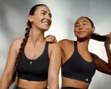 Two women in black sports bras, one with a braid, the other playing with her hair.