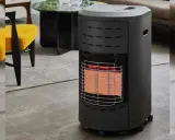 Chauffage d'appoint gaz danger : appareil noir avec grille métallique devant des éléments chauffants rouges, dans un salon moderne.
