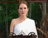 Julianne Moore i den vita klänningen i "Sirens"-serien, med en bakgrund av skog och dekorationer av fjädrar och kvistar.