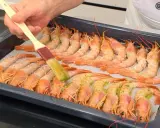 Un pincel baña con aceite y hierbas unos gambones al horno listos para cocinar.