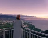 Frau blickt auf weite Landschaft, die ihr Angst vor Urlaub macht. Berge, Meer und Felder im Abendlicht.
