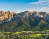 Widok na Tatry z Bachledzkiego Wierchu. Słońce oświetla skaliste szczyty i zielone zbocza, poniżej rozciąga się malownicza wieś.