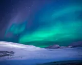 Ett magiskt blått norrsken dansar över en snötäckt fjällvärld under en stjärnklar natt.
