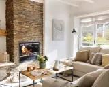 Acogedor salón moderno con chimenea de leña, sofá beige y mesa de centro de madera.