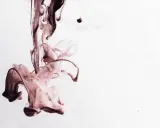 Manchas oscuras y fluidas, como sangrado oscuro entre reglas, se disuelven en un fondo blanco, creando formas etéreas.