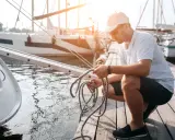 Un homme prépare une corde sur un ponton, la position des bateaux suggère une fin de journée paisible.