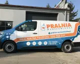 Biało-niebieski van z pomarańczowymi elementami to reklama tranzytowa dla pralni. Na boku widnieje napis "PRALNIA WARSZOWIANKA" i numer telefonu.