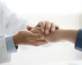 Dłoń lekarza w białym kitlu pociesza dłoń pacjenta. Symbol niepełnosprawności 02-p jest tu metaforą wsparcia.