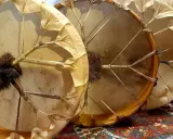 Trois tambours chamaniques, un instrument traditionnel aux peaux tendues et ornées de franges, prêts pour une cérémonie.