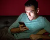 Un hombre joven, con barba, mira su móvil en la oscuridad. Podría ser el perfil de hombres que desaparecen sin dar explicaciones.