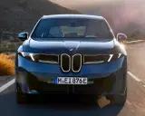 Der BMW iX4 fährt auf einer kurvigen Straße durch eine bergige Landschaft im goldenen Licht der Abendsonne.