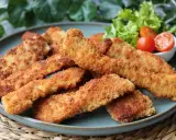 Crujientes fingers de pollo dorados en un plato azul, acompañados de lechuga y tomates cherry. ¡Perfectos para picar!