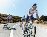 Kolarze jadący w peletonie, pokonując kolejne kilometry Tour de France. Słońce i błękitne niebo towarzyszą im w wyścigu.