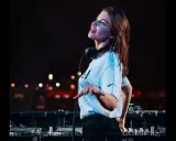 Anfisa Letyago, giovane DJ, con cuffie al collo, mixa musica dal vivo. La sua età è un mistero, ma la sua passione è evidente.