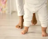 Un bebé da sus primeros pasos, guiado por un adulto. Un momento tierno que ilustra cómo educar a un bebé: con amor y apoyo.