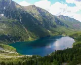 Górskie jezioro otoczone lasem, z wodospadem spływającym po zboczu. Widok przypomina, jak powstało Morskie Oko.