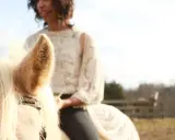 Eine Frau reitet ohne Sattel auf einem hellen Pferd. Ihr Spitzenoberteil und die dunkle Hose sind gut zu erkennen.