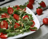 Aromatyczna sałatka z truskawkami, rukolą, serem feta i migdałami na białym talerzu.