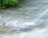Czyszczenie tarasu z płyt betonowych myjką ciśnieniową. Woda spływa po mokrych płytkach, tworząc pianę.