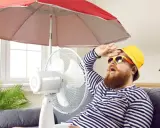 Un homme transpire sous un parasol, ventilateur et plante pour comment rafraichir sa maison. Il a chaud.