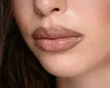 Labbra carnose e lucide, con un effetto naturale per ingrandire le labbra, evidenziate da un rossetto nude.