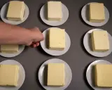 Neun Butterstücke auf Tellern, ein Mann greift nach einem. Die Butter zutaten sind bereit für einen Test.