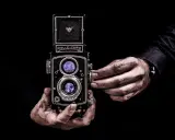 Dwie ręce trzymają aparat Rolleiflex, jedna reguluje ostrość. Sztuka fotografii, zasada złotego środka w kadrze.