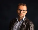 Jacek Bartosiak, autor książek, w okularach i skórzanej kurtce, patrzy w obiektyw.