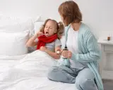 Bambina malata a letto prende sciroppo, mentre la mamma tiene il flacone. Forse per febbre o tosse, un mix di brufen e tachipirina insieme per farla stare meglio.