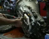 Mecánico trabajando en un motor y caja de cambios, con aceite rojo derramado en la mesa.