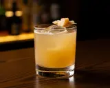 En gyllene penicillin drink med is och en garnering av ingefära på en träyta.