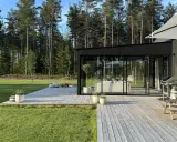 Enkel uteplats med trätrall och glaspartier som vetter mot en grönskande skog. Perfekt för avkoppling.
