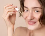 Une femme souriante applique une goutte de sérum à la vitamine C sur son visage. C'est le moment idéal pour utiliser la vitamine C sur le visage pour une peau éclatante.