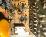 Uszkodzony opornik z czerwonym okręgiem na płytce drukowanej, obok innych elementów elektronicznych.