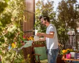 Un homme arrose une plante brise-vue qui pousse vite en bac sur son balcon ensoleillé.
