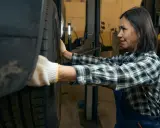 Mechaniczka w rękawiczkach sprawdza oponę, słysząc niepokojące stukanie w kole.