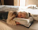 Ein kleines Mädchen kuschelt sich auf einem Bett an ein Kissen. Die Schlafphasen von Kindern sind wichtig für ihre Entwicklung.
