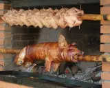 Ein Spanferkel grillen über offenem Feuer. Darüber hängen mehrere Hähnchen am Spieß.