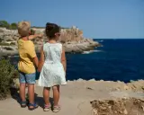 Två barn står vid havet, redo för sommarlåtar och skolavslutning. Pojken pekar mot horisonten.