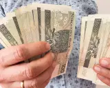 Ręce trzymające plik banknotów 100 zł. Planowanie finansowe, jak wybrać najkorzystniejsze lata do emerytury, wymaga analizy oszczędności.