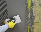 Ręka w żółtej rękawicy rozprowadza zaprawę, zatapiając siatkę. Dobry klej do zatapiania siatki jest kluczowy.