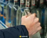 Dłoń sięga po butelkę wódki, a artykuł na medonet.pl analizuje wpływ alkoholu, w tym piwa, na białe krwinki.