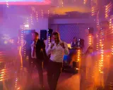 Wesołe uroczystości weselne inaczej! Dwóch mężczyzn tańczy w świetle dyskotekowej kuli i kolorowych świateł, DJ gra muzykę w tle.