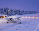 Ett litet flygplan står på en snötäckt flygplats i skymningen. Ljus längs landningsbanan lyser upp vägen mot norr, redo för resan från Stockholm till Lappland.