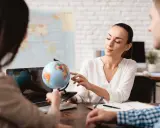 Praca w biurze podróży: konsultantka pokazuje klientom na globusie miejsca na wakacje.